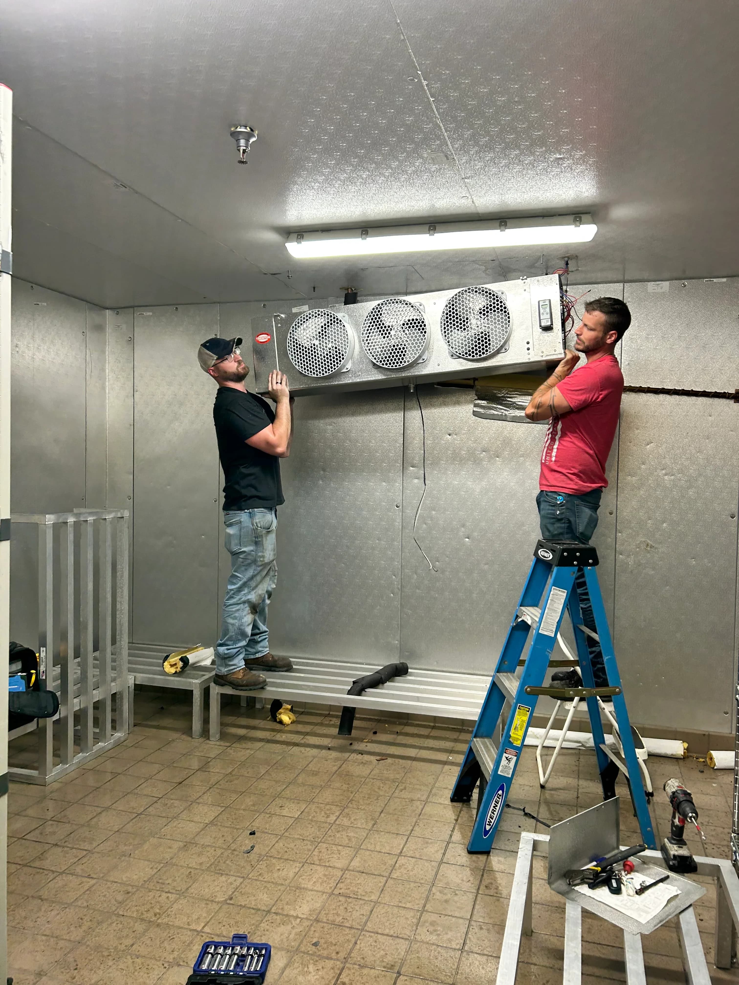 Technicians mounting a walk-in cooler evaporator during an installation